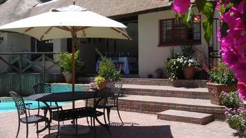 Un patio exterior con mesa y sillas, una piscina y plantas en macetas.