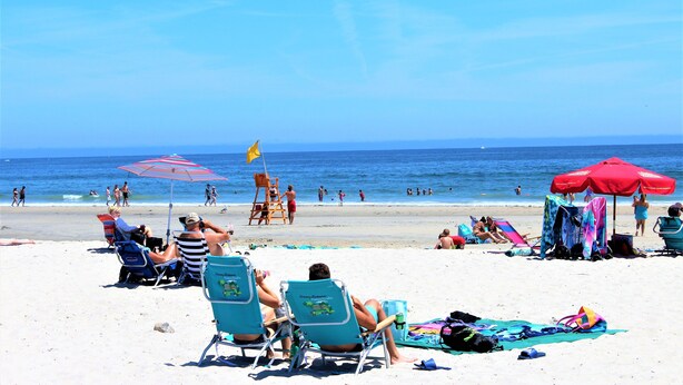 Una platja amb gent relaxant-se en gandules i ombrel·les, una torre de socorrises i l'oceà al fons.