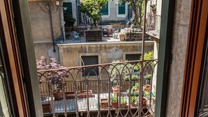 Ein Balkon mit schmiedeeisernem Geländer, Pflanzkübeln und Blick auf benachbarte Gebäude.