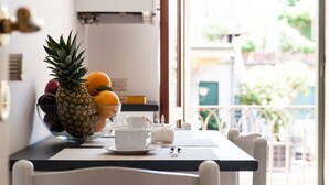 Ein Esstisch mit einer Obstschale, die eine Ananas, Orangen und Äpfel enthält, einer weißen Tasse und einer kleinen weißen Kanne.