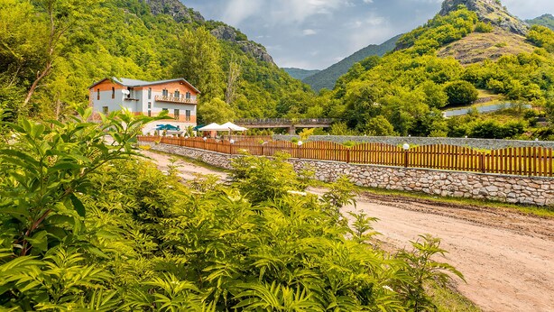 Un hotel con pared de piedra y valla de madera, rodeado de abundante vegetación y montañas.