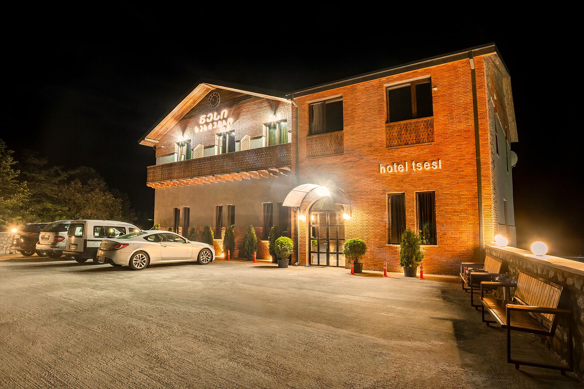 A two-story hotel with a brick facade, a visible entrance, and a parking area with cars.