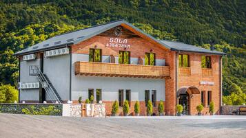 A hotel with a brick facade, a balcony, and a mountain backdrop.
