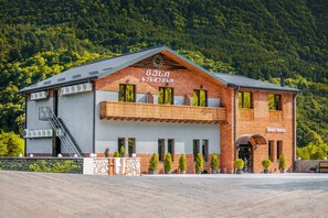 Un hotel con facciata in mattoni, un balcone e montagne sullo sfondo.