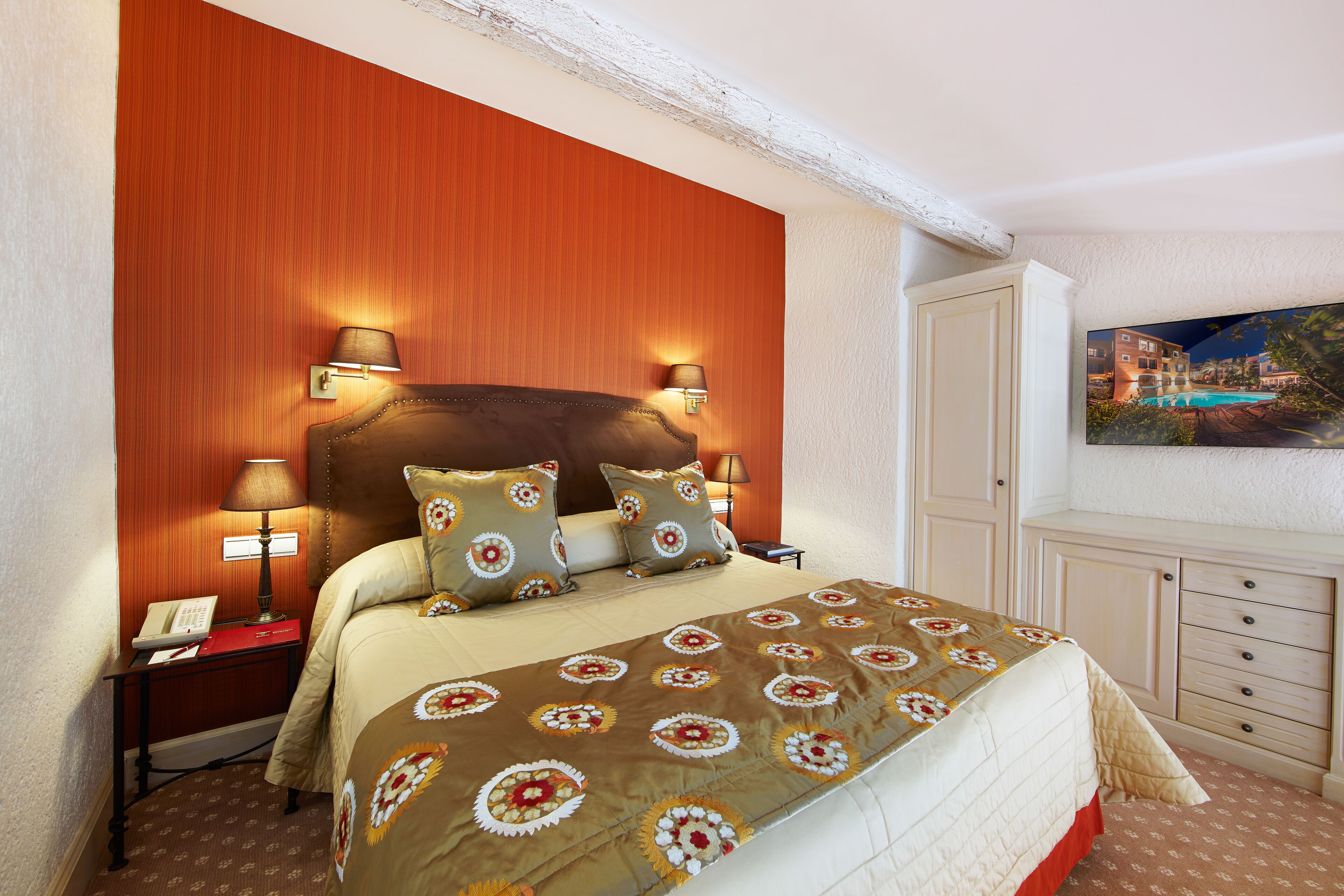 Een hotelkamer met een groot bed, twee bedlampen, een nachtkastje met een telefoon en een schilderij aan de muur.