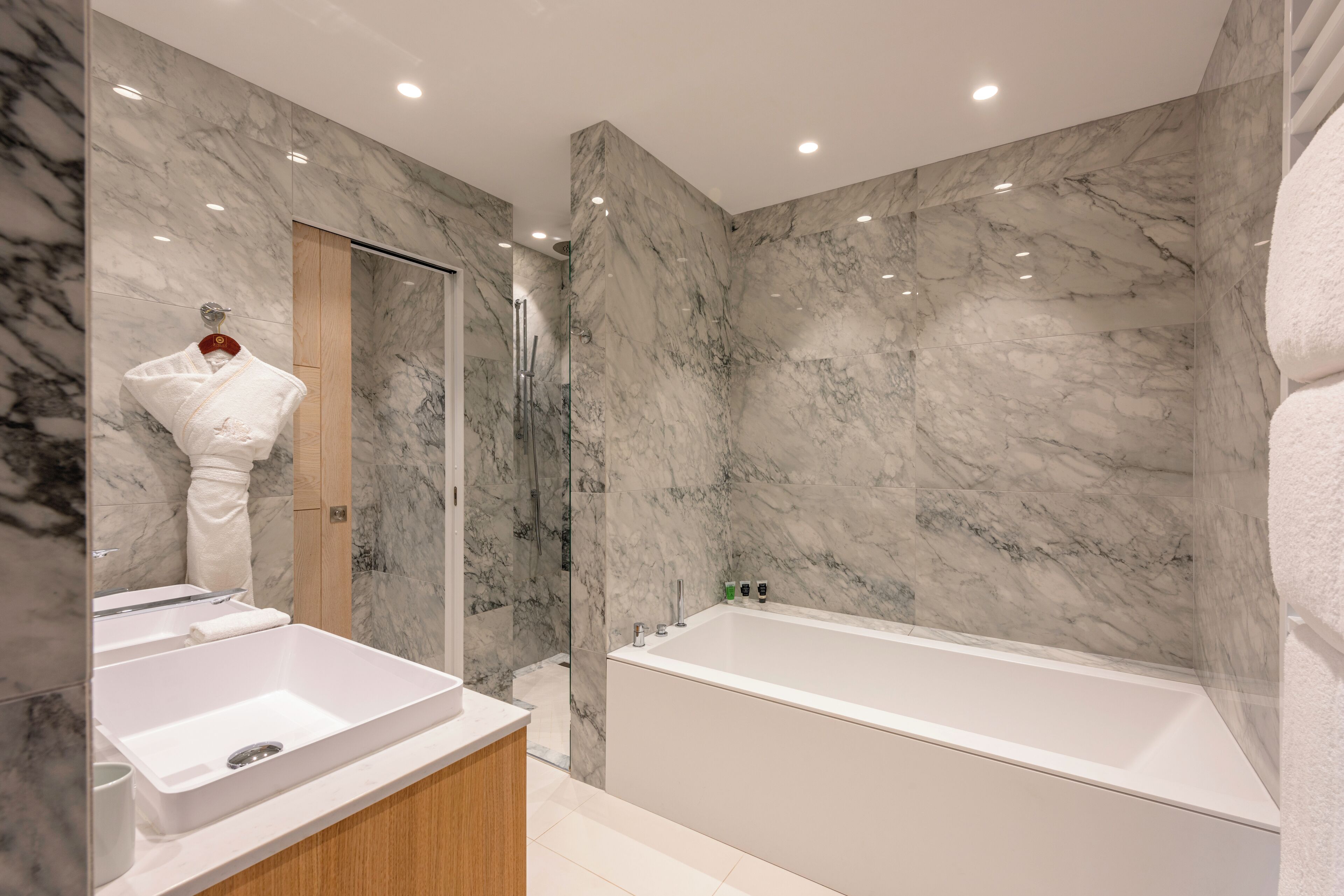 A modern bathroom with marble walls, a bathtub, and a double sink.