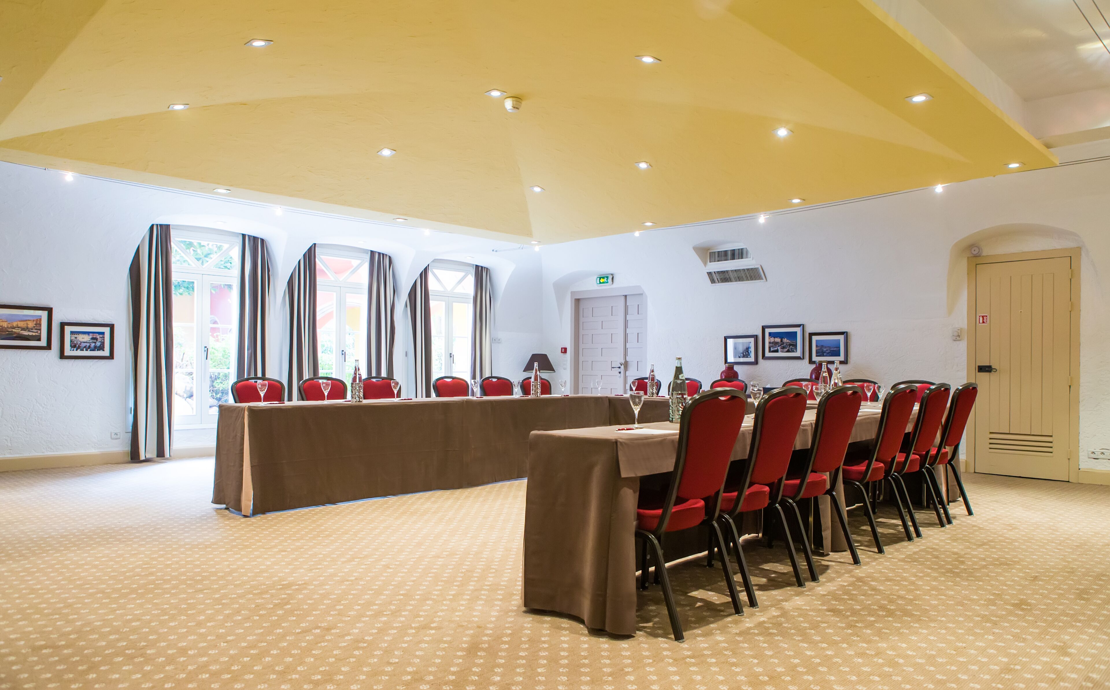 A conference room with a long table, red chairs, and a beige carpet.