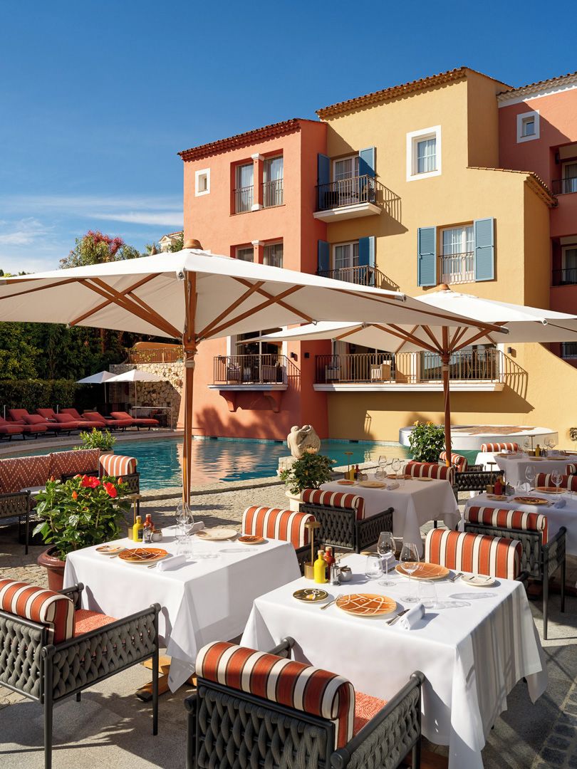 Area pranzo a bordo piscina con tavoli apparecchiati per due, sedute all'aperto e una piscina sullo sfondo.