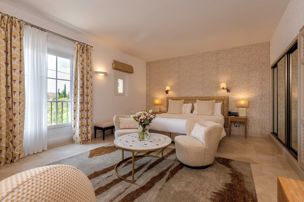 Een hotelkamer met een groot bed, een ronde salontafel, een bank en een tafeltje met een bloevas.