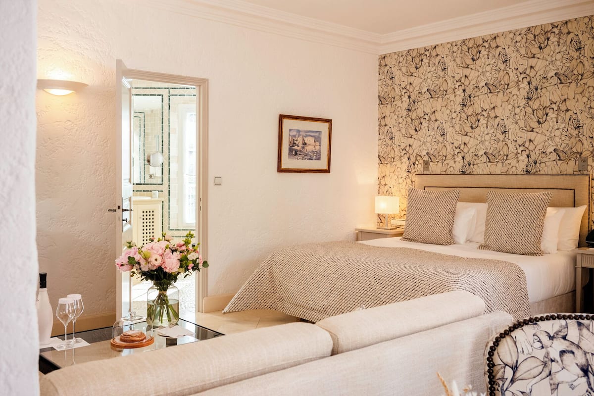 Een hotelkamer met een bed, een slaapbank, een klein tafeltje met een bloevas en een lijst op de muur.