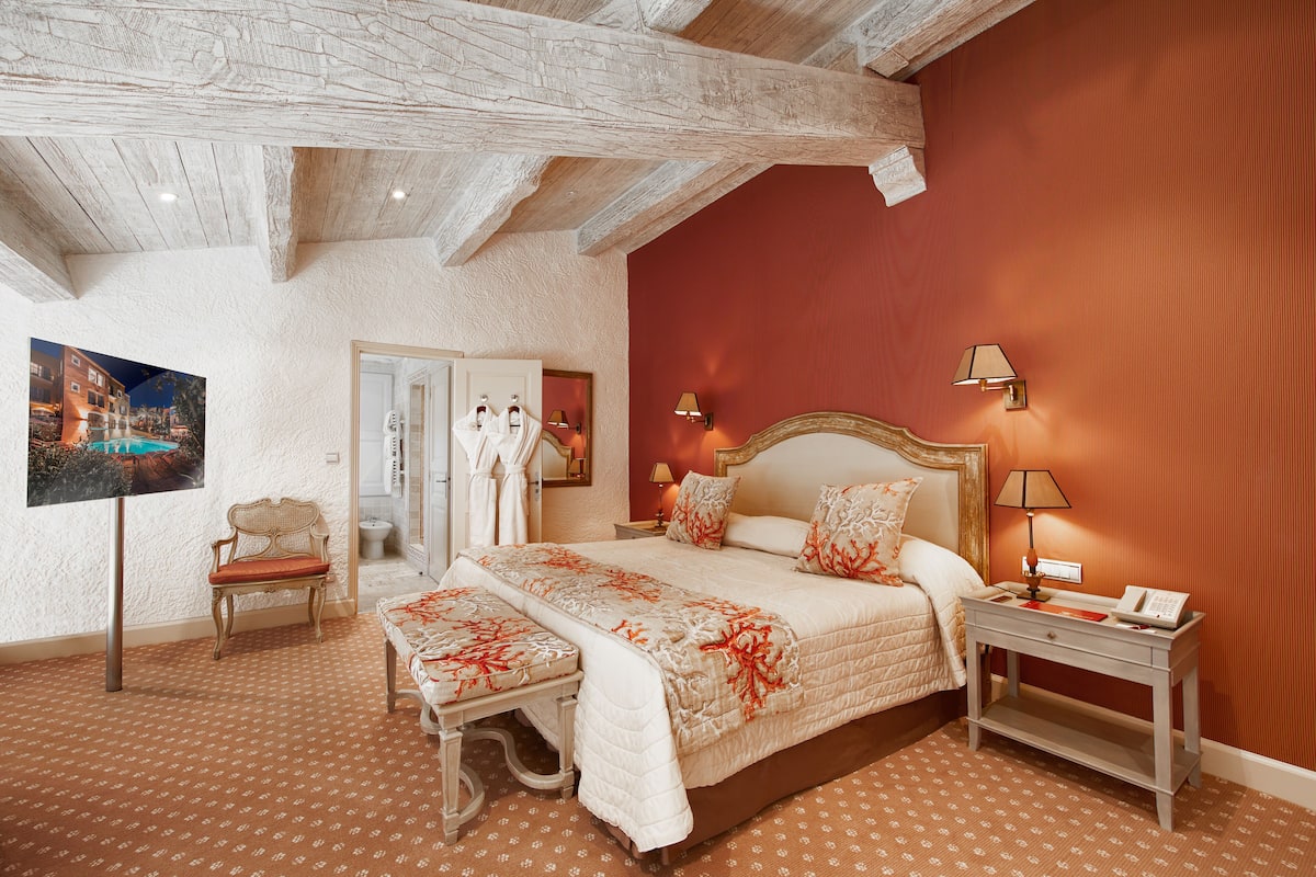 Een slaapkamer met een groot bed, een bankje, een nachtkastje en een schilderij aan de muur.