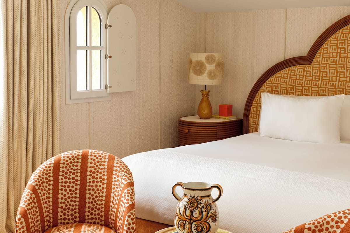 Een hotelkamer met een groot bed, twee fauteuils, een tafeltje, een lamp en een decoratieve vaas.