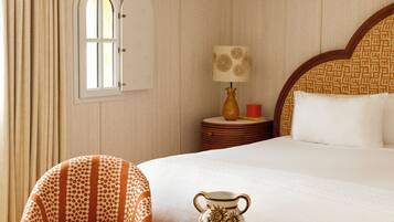 Une chambre d’hôtel avec un grand lit, deux fauteuils, une petite table, une lampe et un vase décoratif.