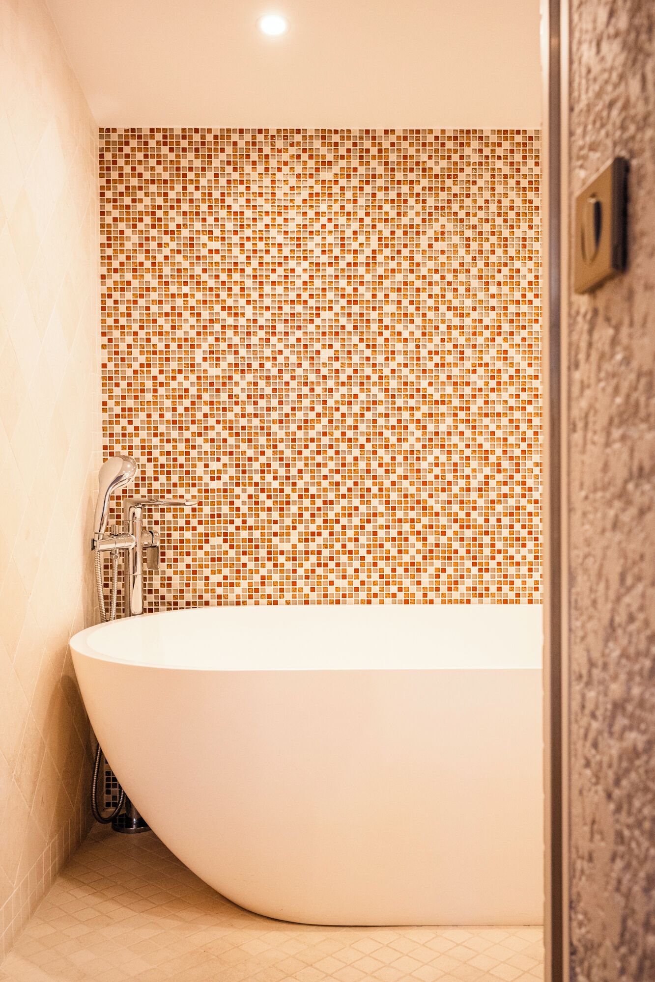 Une salle de bain moderne dotée d’une grande baignoire sur pied, d’un espace douche avec un pommeau de douche à main et d’un mur recouvert de mosaïques.