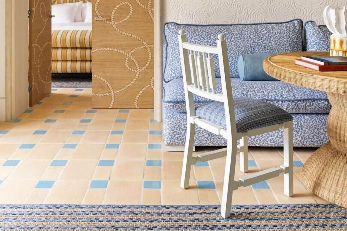 Een kamer met een patroon vloer, een blauwe bank, een houten stoel en een bed met gestreepte dekbedden.