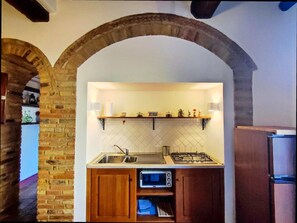 Compact kitchen with exposed brick walls, wooden archway, and modern amenities for basic meal preparation.