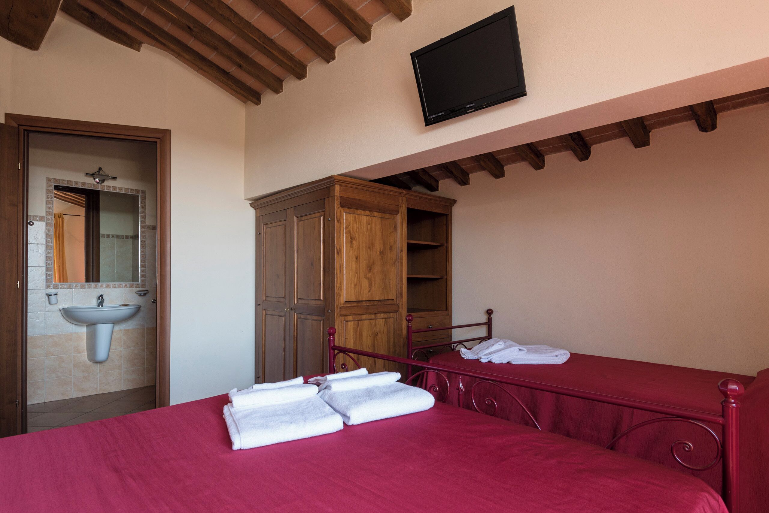 Una camera da letto con un letto, un armadio in legno, un lavandino e una televisione appesa al muro.