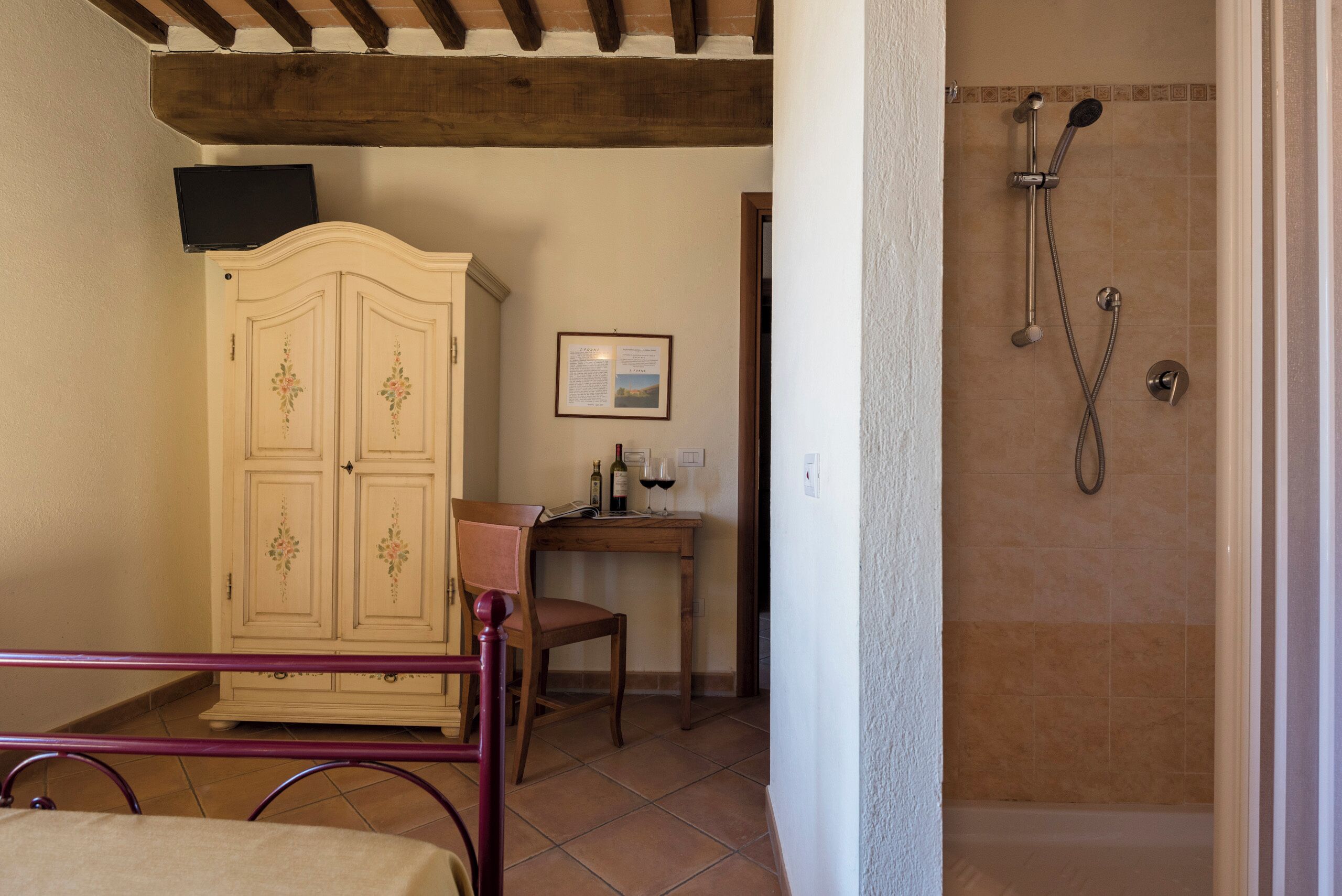 Un baño con ducha, un armario de madera, una silla y una mesita con una botella de vino y copas.