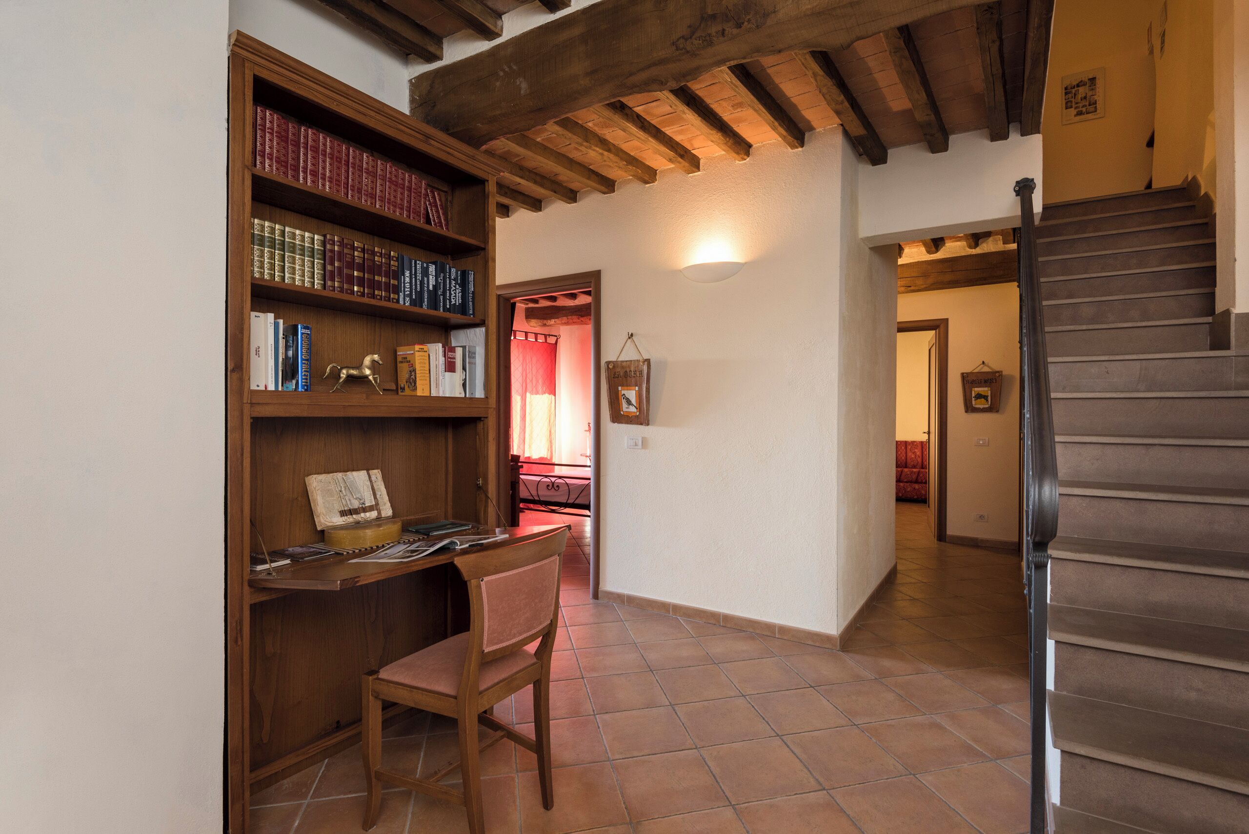 A study area with a wooden desk, chair, and bookshelf. A staircase is visible to the right.