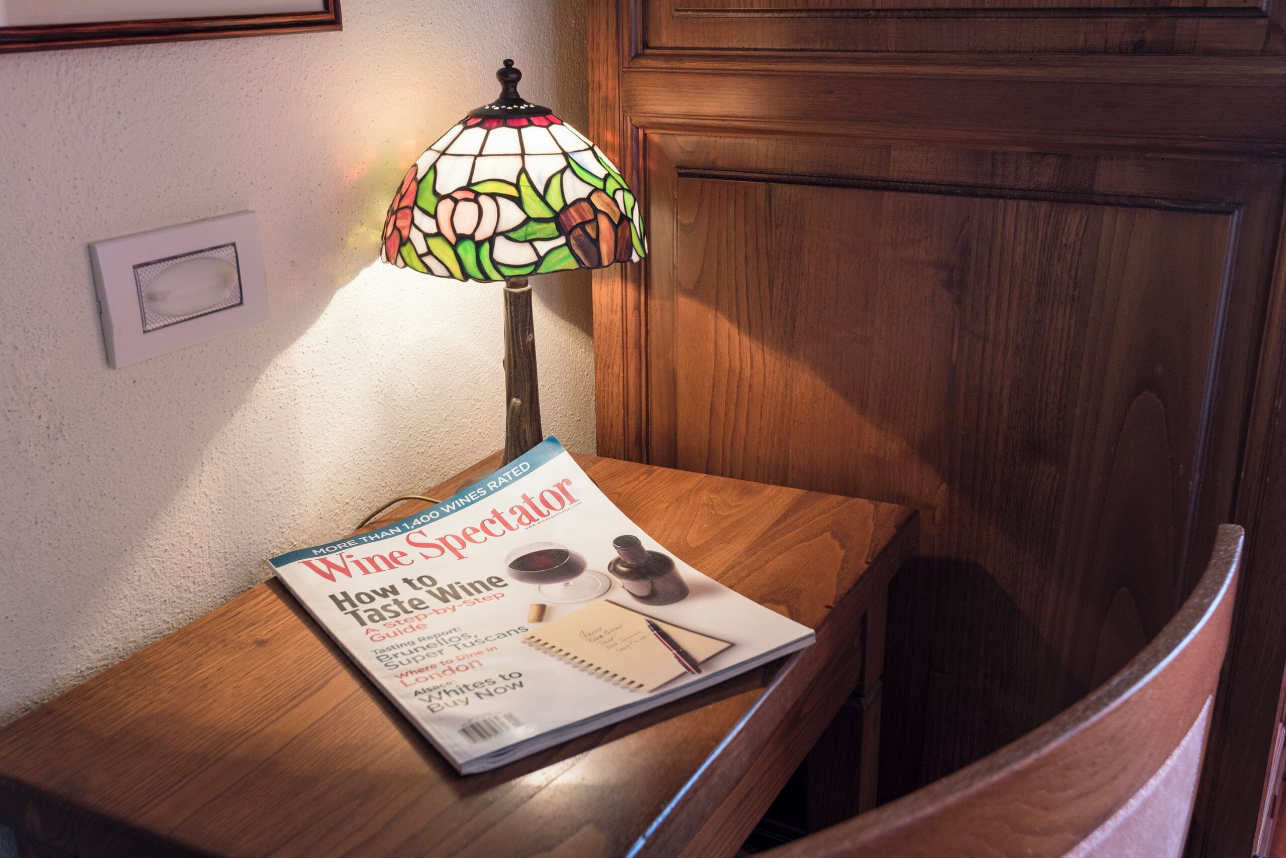 Una revista titulada "Wine Spectator" sobre una mesa de madera, junto a una lámpara de vitral.