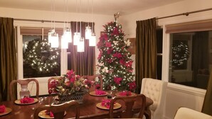 Een eetkamer met een kerstboom, een kroonluchter en een raam met gordijnen.
