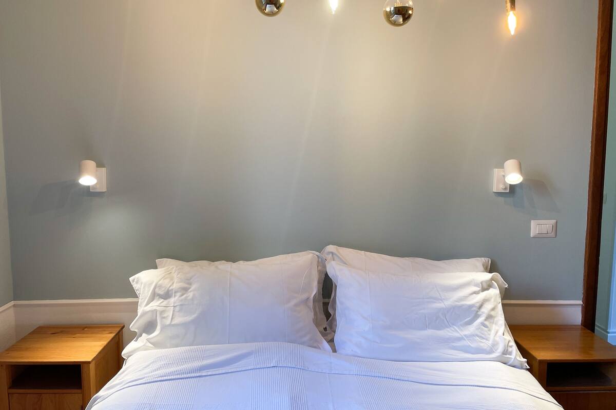 A neatly made bed with white linens, two bedside tables, and wall-mounted light fixtures.