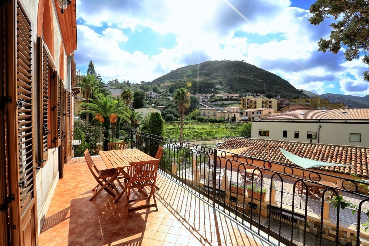 A balcony with a wooden table and chairs, overlooking a hillside with buildings and greenery.