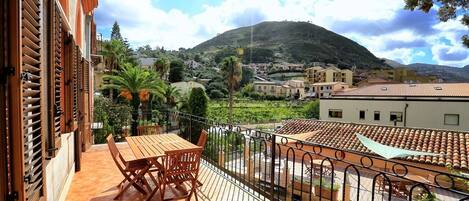 A balcony with a wooden table and chairs, overlooking a hillside with buildings and greenery.