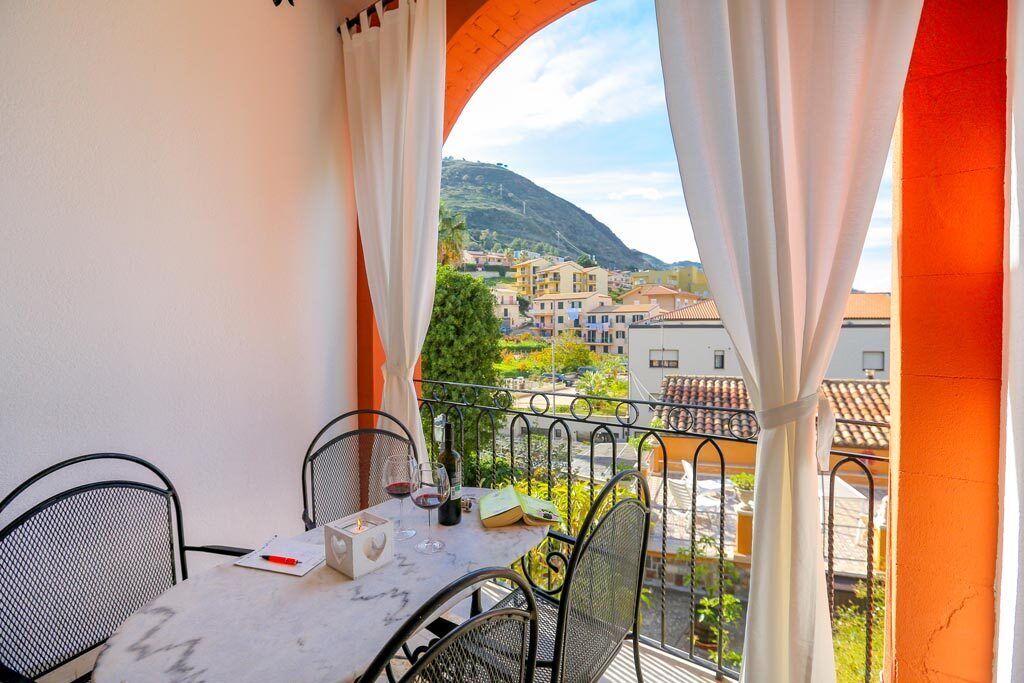 Un balcón con mesa y sillas, con vistas a una colina con edificios.