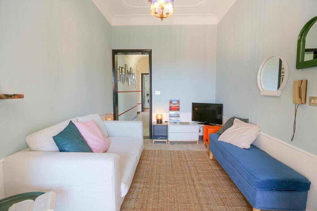 Un salon avec un canapé blanc, un canapé bleu, un téléviseur et une petite table avec une lampe.