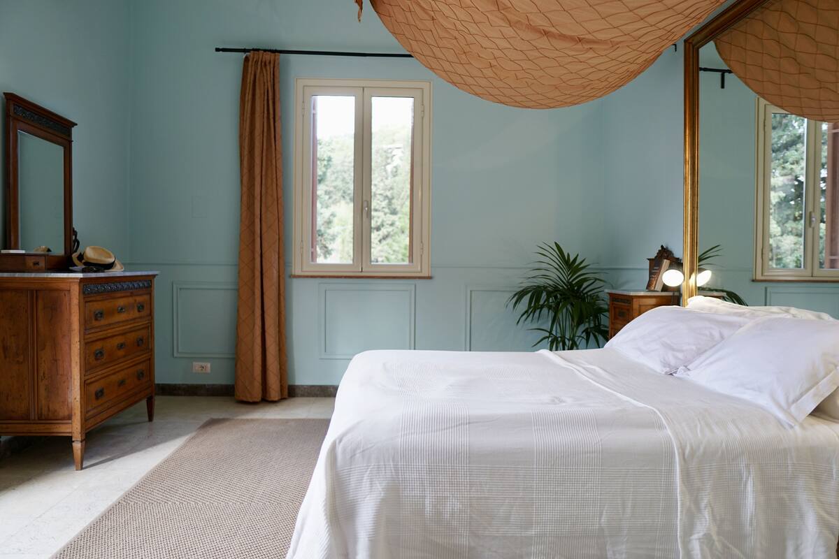 A bedroom with a bed, dresser, mirror, window, and curtains.