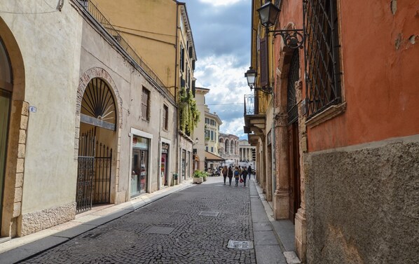 A cobblestone street lined with historic buildings, including a building with a large arched doorway and another with a barred window. - Arena di Verona Rensi Italianflat (Verona)