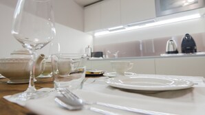 A dining table set with white tableware, including a glass, teapot, cups, and plates, in a modern kitchen with white cabinets and stainless steel appliances. - Arena di Verona Rensi Italianflat (Verona)