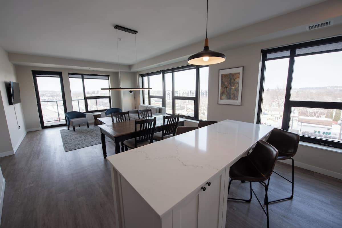 A modern kitchen with a large island, dining area, and large windows offering city views.