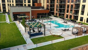 A rooftop pool area with lounge chairs and umbrellas, surrounded by a modern building with a brick facade.