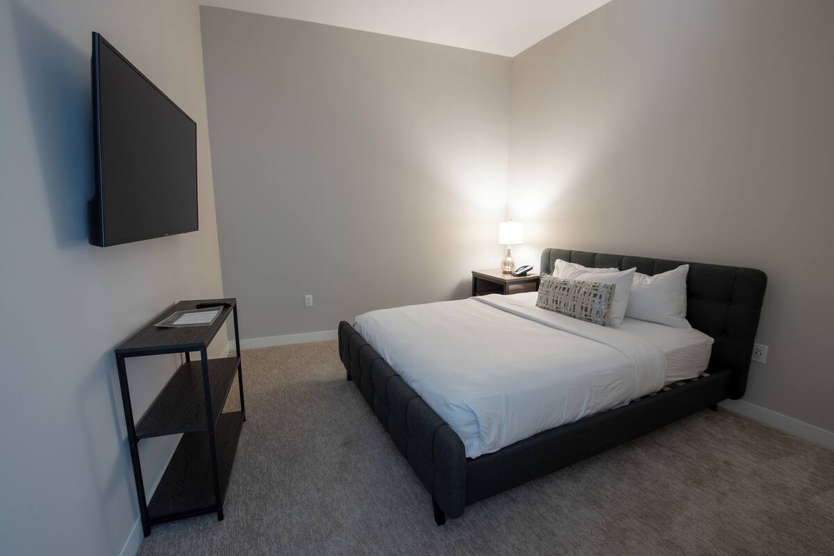 A bedroom with a bed, a nightstand, a lamp, and a TV mounted on the wall.