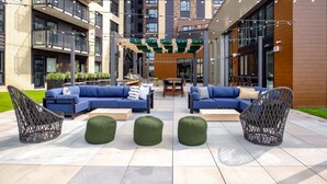 Un espace extérieur aménagé avec des canapés bleus et des fauteuils en osier, une table en bois et des poufs verts sur une terrasse carrelée.