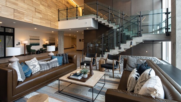 Un vaste espace de vie agrémenté d’un escalier moderne, de canapés en cuir et d’un éclairage contemporain.