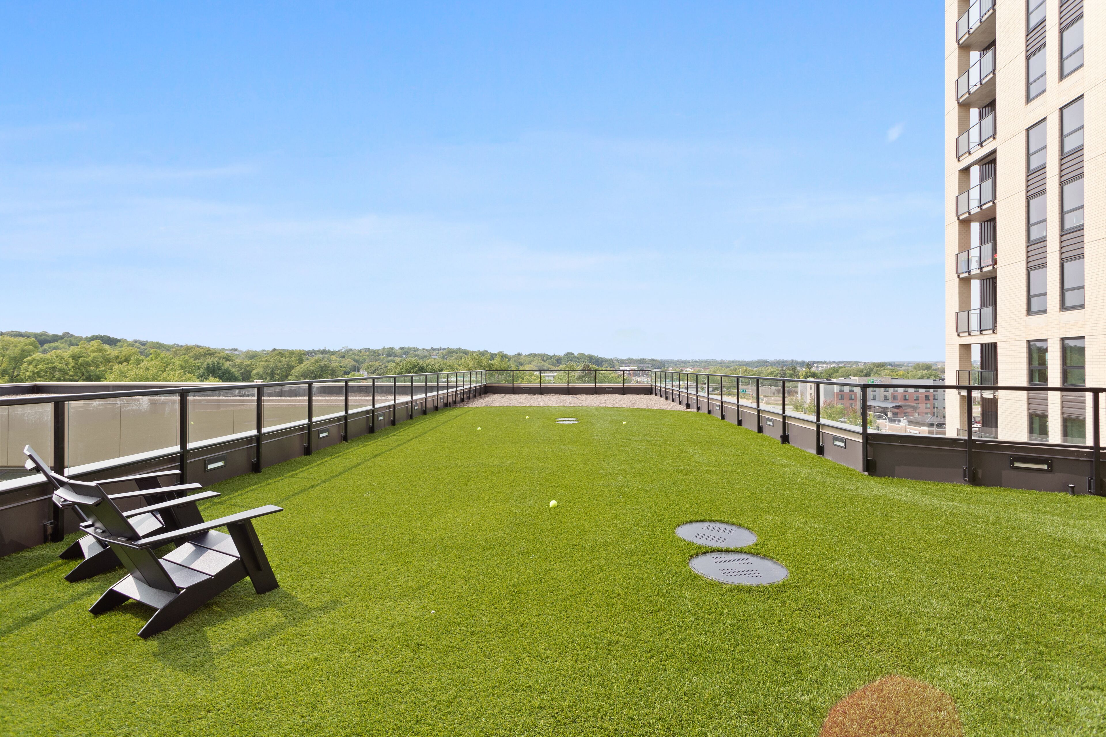 A rooftop terrace with artificial grass, seating, and a view of the city.