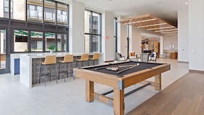 Une table de billard moderne dans une pièce spacieuse et bien éclairée, dotée de grandes fenêtres et d’un coin bar.