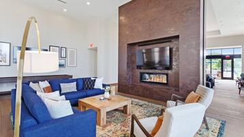 A modern living room with a blue sofa, white armchairs, a wooden coffee table, and a fireplace.