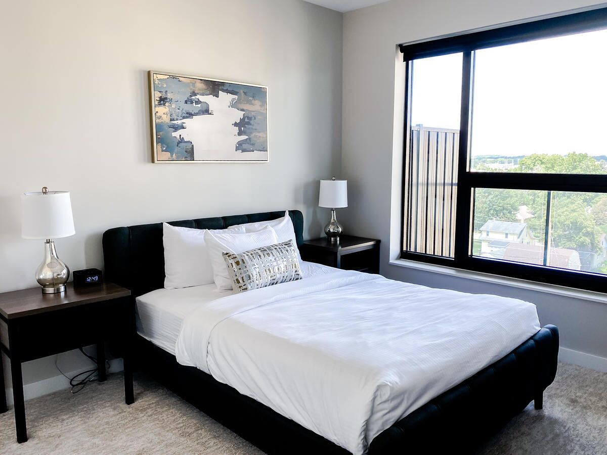 A neatly arranged bedroom with a large bed, two bedside tables, and a window offering a city view.