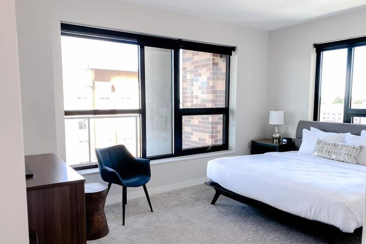 A hotel room with a large bed, a desk, a chair, and a window with a view of a brick building.