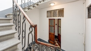 Una escalera con barandillas metálicas decorativas y un pasamanos de madera, que conduce a una habitación con piso de tablones y una puerta de madera.