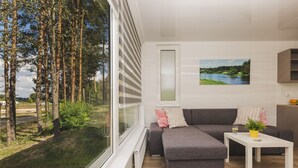A modern living room with a grey sectional sofa, a white coffee table, and a view of a forest through large windows. - Resort Stara Wieś (Patnów)