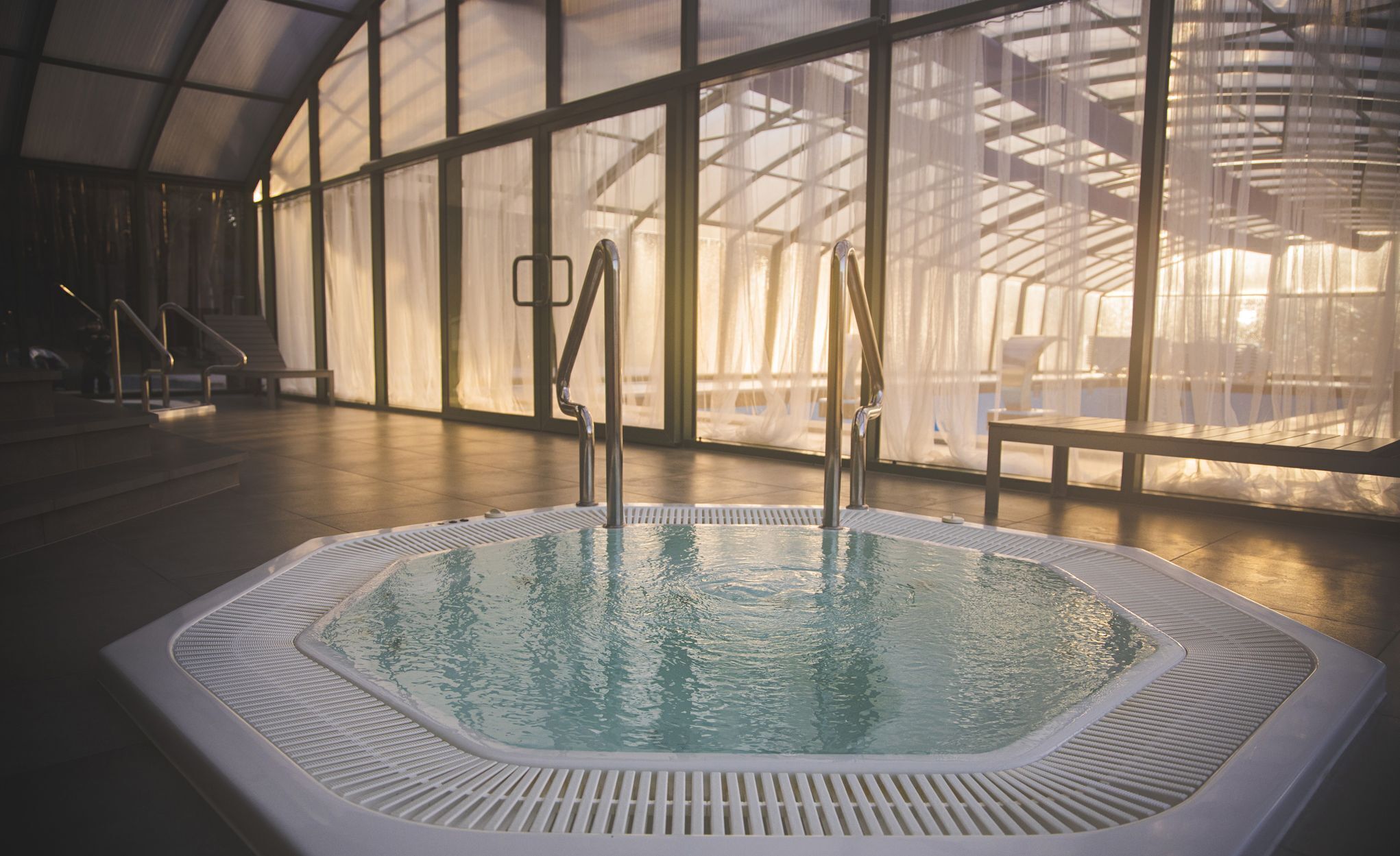 A large indoor swimming pool with clear water, surrounded by glass walls and a high ceiling.