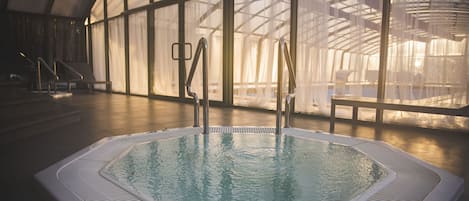 A large indoor swimming pool with clear water, surrounded by glass walls and a high ceiling.