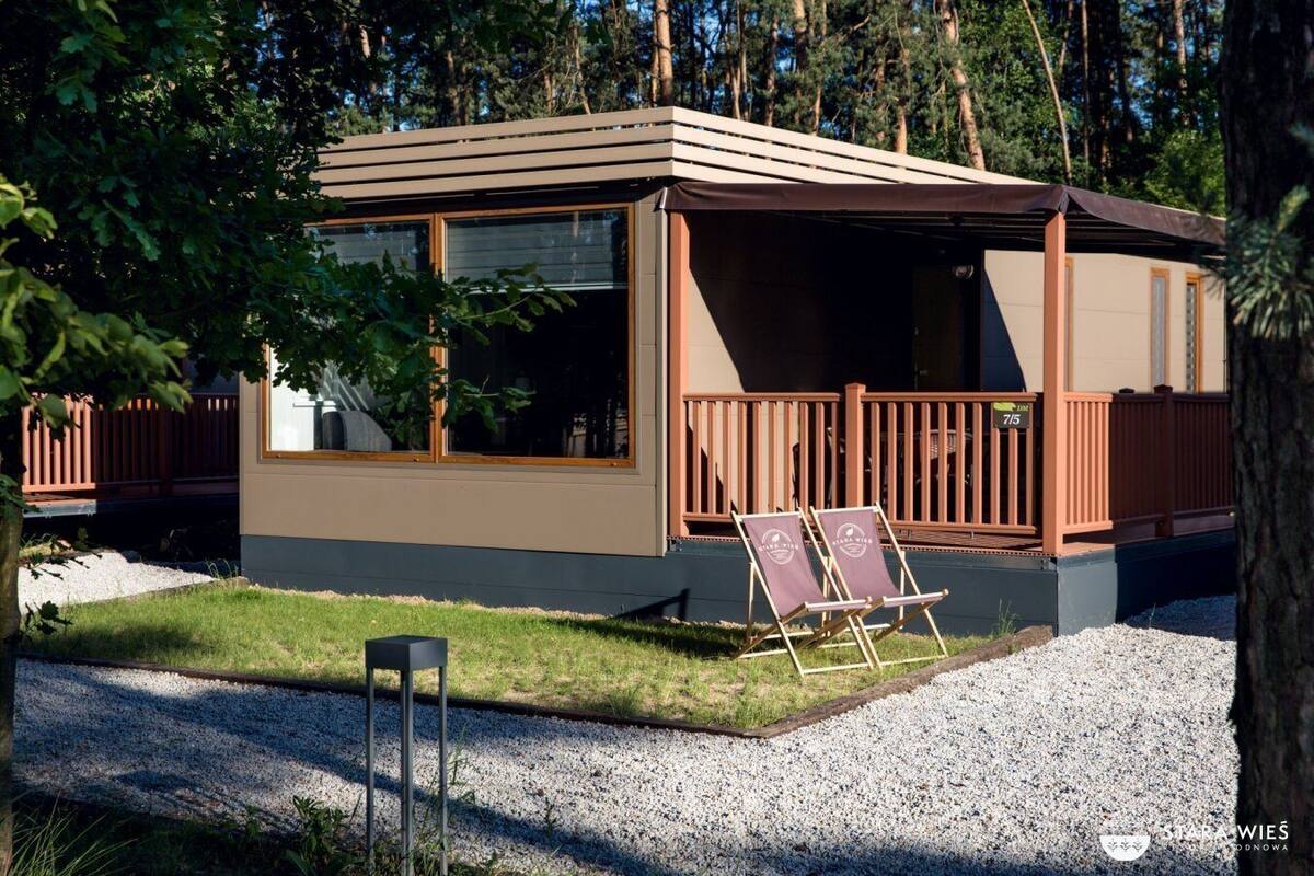 A cabin with a deck, two chairs, and a gravel path.