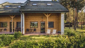 A wooden cabin with a tiled roof, large windows, and a patio area with outdoor seating. - Resort Stara Wieś (Patnów)