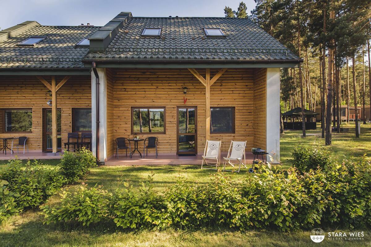 A wooden cabin with a tiled roof, large windows, and a patio area with outdoor seating.